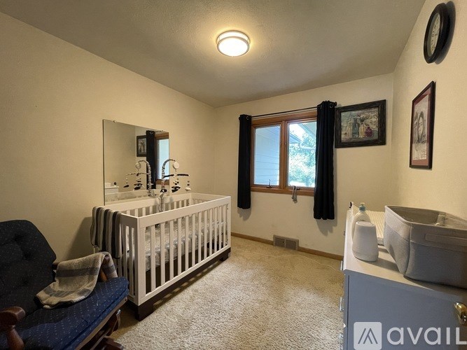 A baby's room with a crib, a chair, and a window with black curtains.