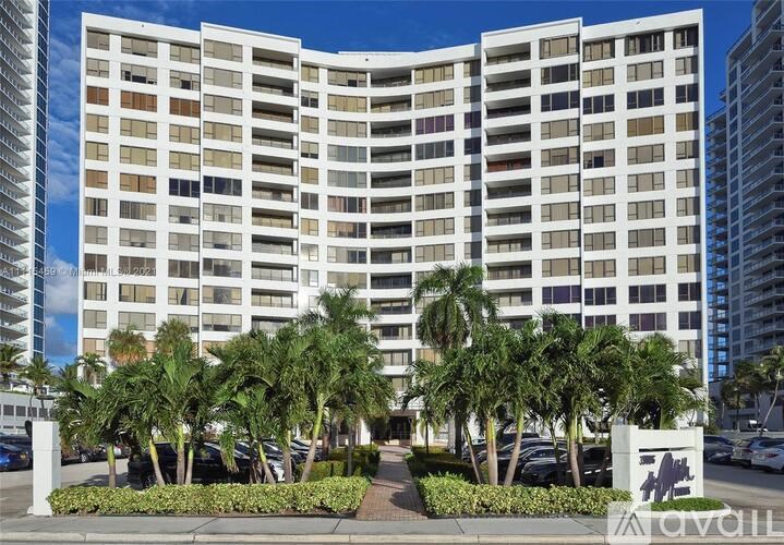 A tall white building with balconies and palm trees in front.