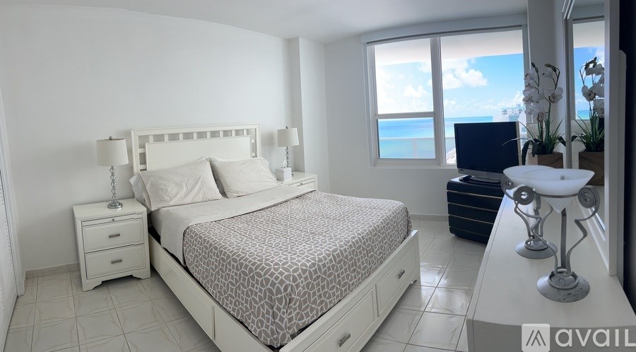 A bedroom with a large bed, a nightstand, and a window overlooking the ocean.