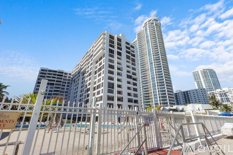 A white fence surrounds a pool in front of a large building.