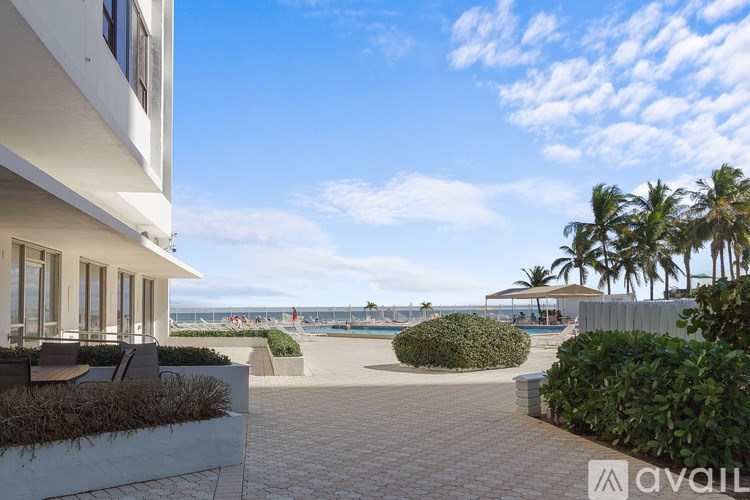 A sunny day at the beach with a building on the left and palm trees in the background.