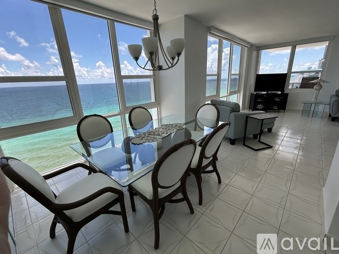 A living room with a glass table and chairs overlooking the ocean.