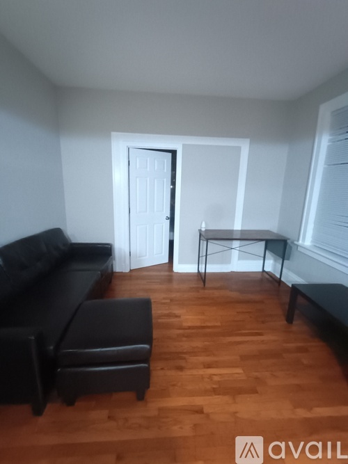 A black couch and ottoman are in a room with a wooden floor and white walls.