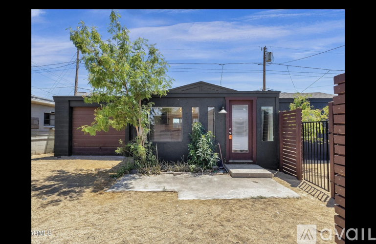 A small house with a brown door and a tree in front.