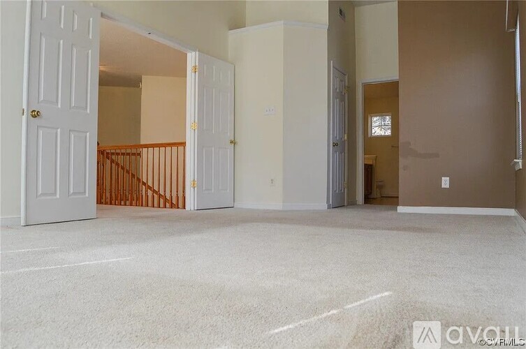 A spacious living room with a carpeted floor and a staircase leading to another room.