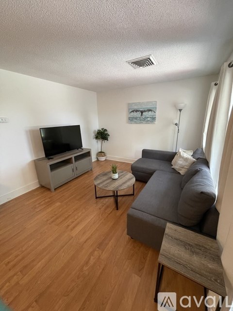 A living room with a grey couch, a wooden floor, and a painting on the wall.