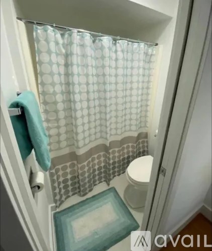 A white toilet with a blue towel and a shower curtain with circles on it.