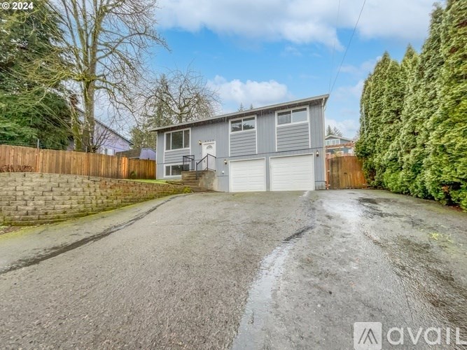 A grey house with a white garage door is surrounded by a wooden fence and greenery.