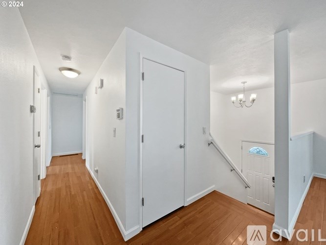 A hallway with white walls and wooden floors leading to a staircase.