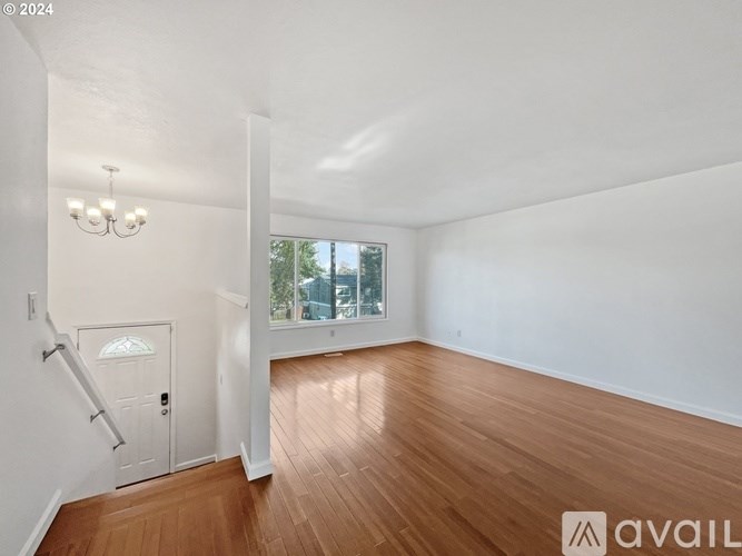 A room with wooden floors and white walls, a chandelier, and a door leading to a balcony.
