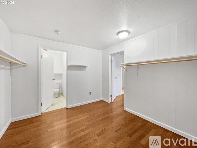 A room with wooden floors and white walls, with a toilet visible in the doorway.