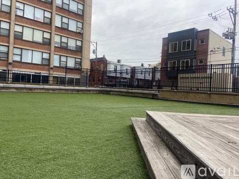 A green artificial turf soccer field with a wooden platform in front of a brick building.