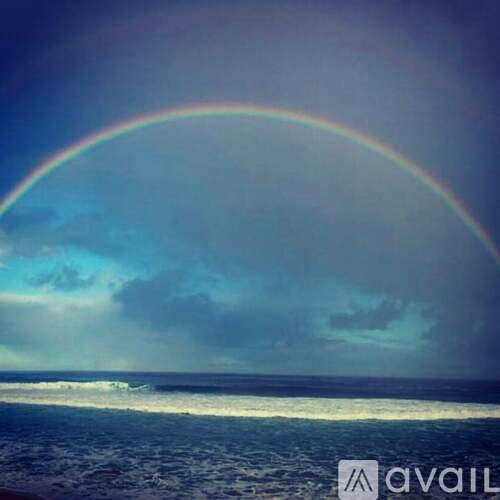 A rainbow arches over a cloudy sky over a beach.