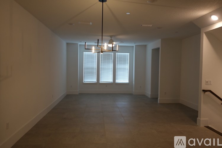 A large empty room with a chandelier and a window with blinds.