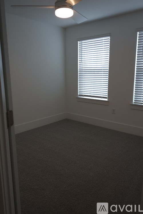 A room with a carpeted floor and two windows with blinds.
