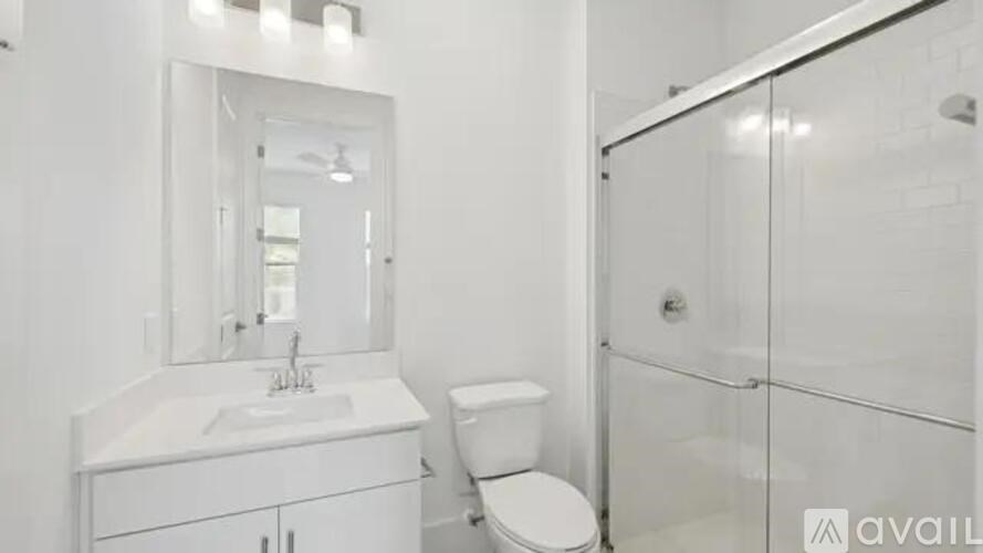 A white bathroom with a toilet, sink, mirror, and shower.