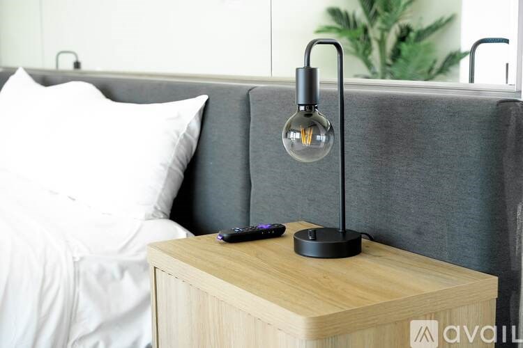 A modern bedroom with a grey headboard and a wooden nightstand with a lamp on it.