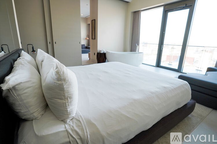 A bed with white pillows and a white bedspread in a room with a view of the city.