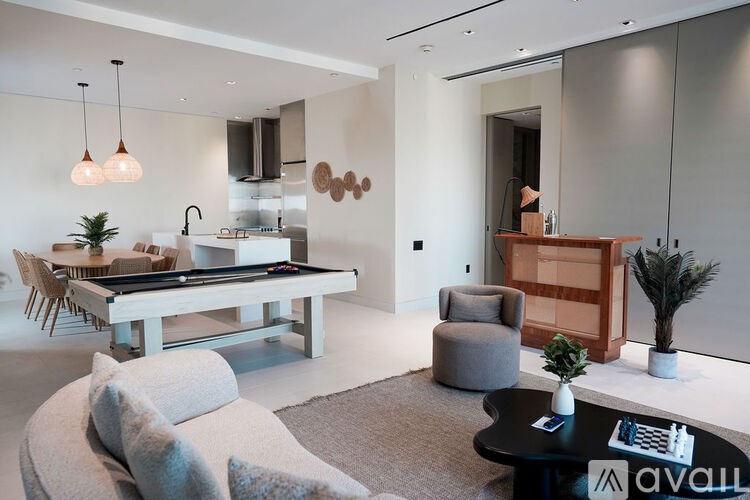 A modern living room with a pool table and a kitchen area in the background.