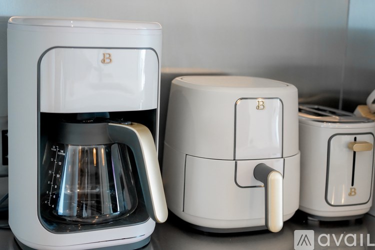 A white coffee maker with a glass carafe and a white coffee pot with a gold handle.