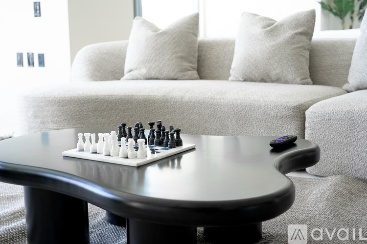 A chess board with pieces on it sits on a coffee table in front of a couch.