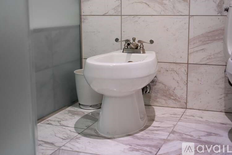 A white pedestal sink with a chrome faucet in a marble tiled bathroom.