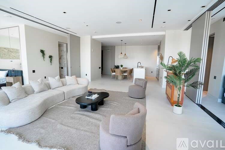 A modern living room with a large sofa, a coffee table, and a dining area in the background.