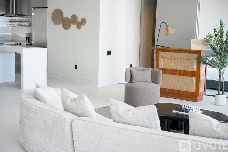 A living room with a white couch, a grey armchair, a wooden cabinet, and a potted plant.