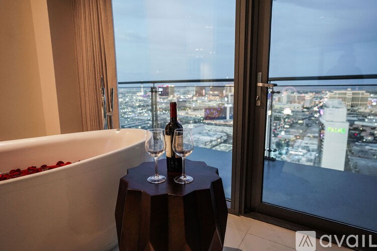 A bottle of wine is on a table next to a bathtub with rose petals in it.