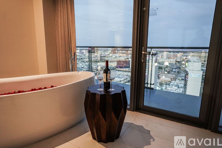 A bathroom with a tub full of rose petals and a bottle of wine on a table.