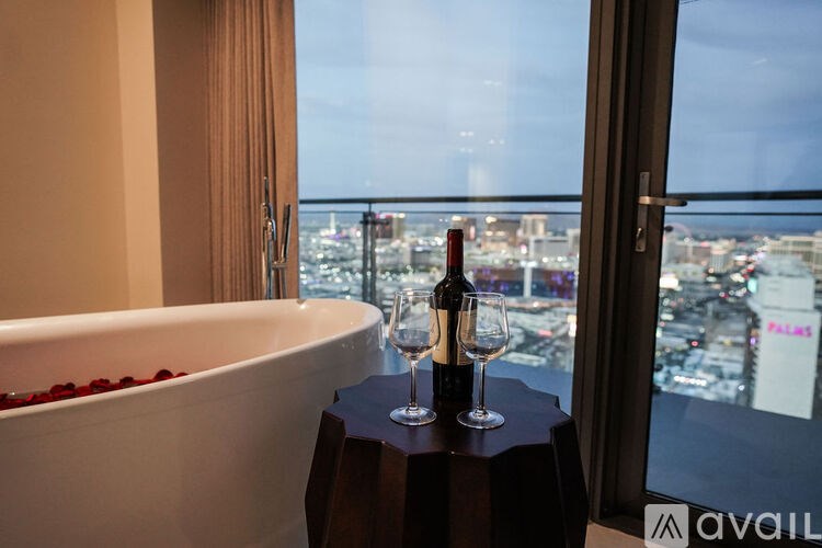 A bottle of wine is on a table next to a bathtub with rose petals.