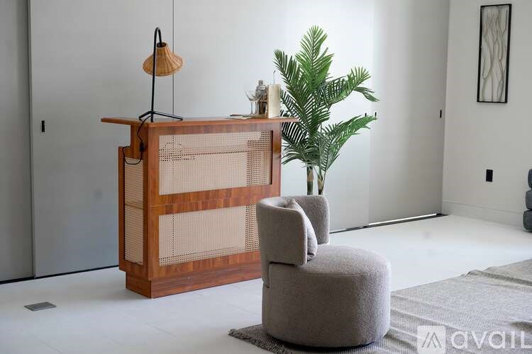 A wooden cabinet with a mesh screen door is next to a grey armchair in a room with a plant and a lamp.