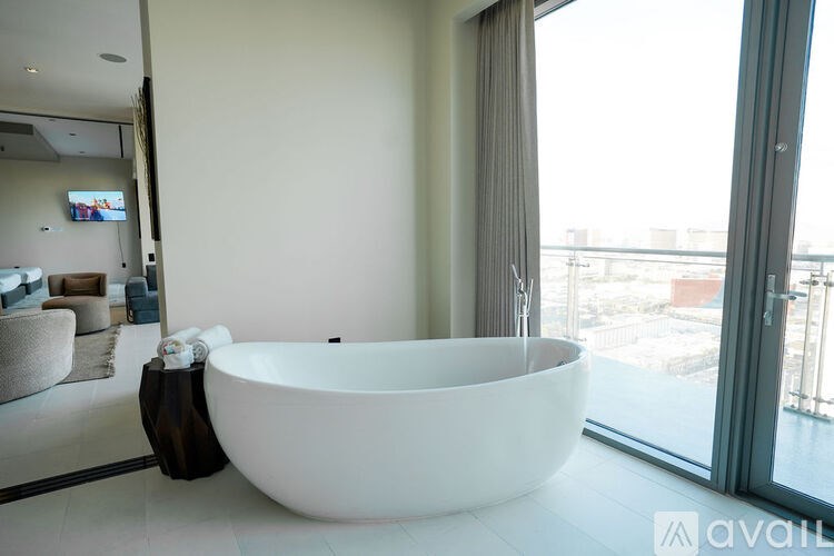 A white freestanding bathtub is in a modern bathroom with a view of the city.