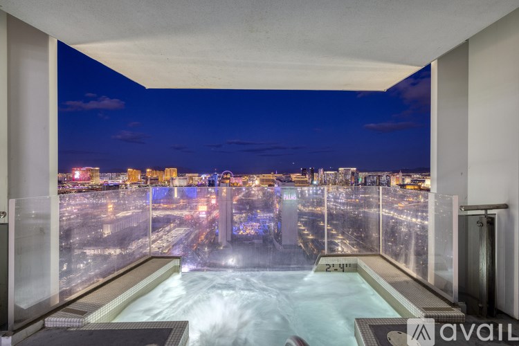 A hot tub is in the middle of a room with a view of the city at night.