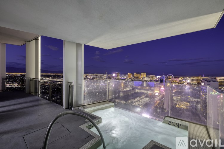 A balcony with a hot tub overlooking a city at night.