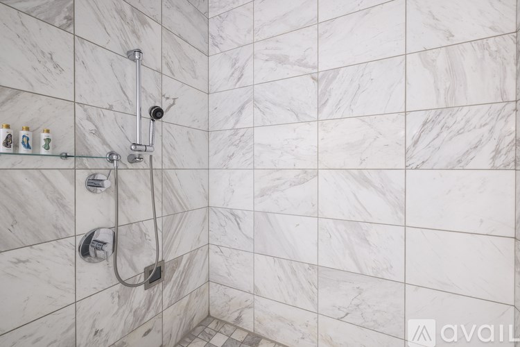 A shower area with a marble tile wall and a glass door.