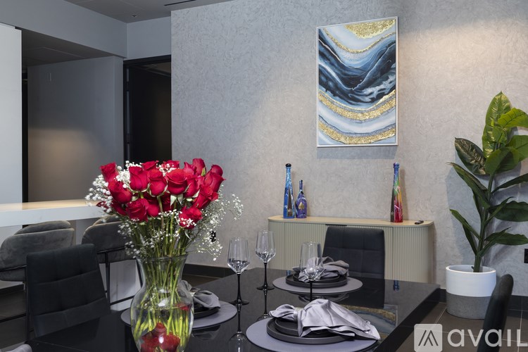 A dining table set with a vase of red roses in the foreground.