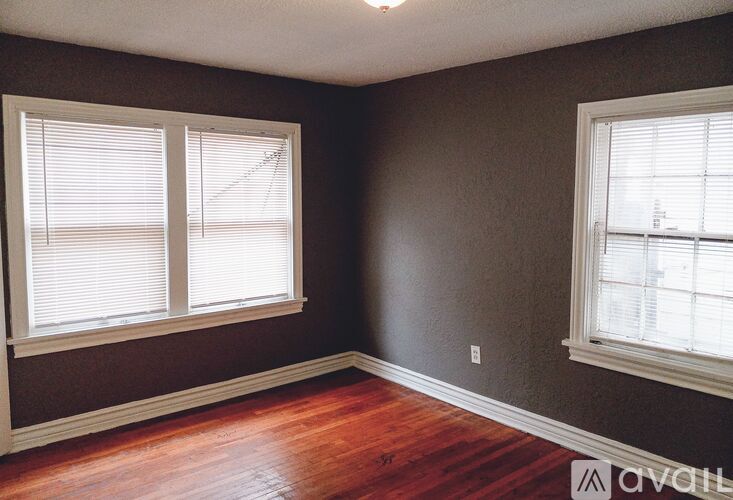 A room with wooden floors and two windows with blinds.