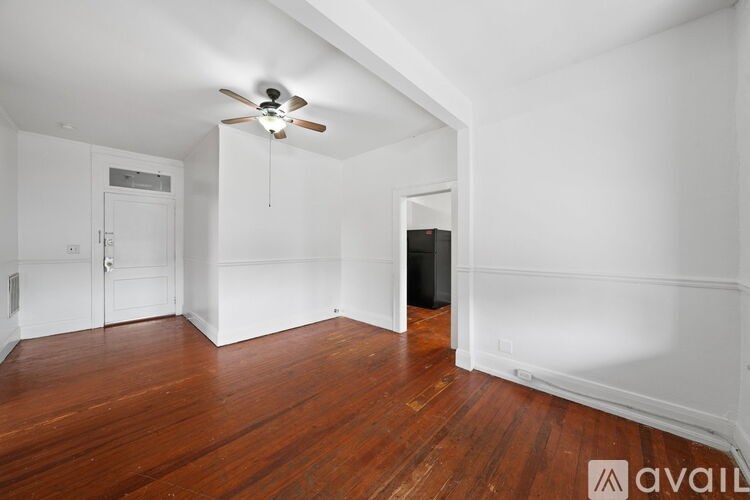 A room with wooden floors and white walls, a ceiling fan, and a door leading to another room.
