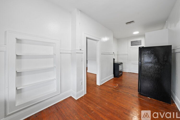 A black fridge sits in a room with wooden floors and white walls.