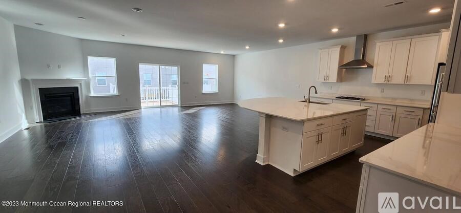 A large, empty living room with a fireplace and a kitchen area with white cabinets.
