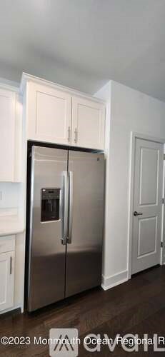 A stainless steel refrigerator in a kitchen with white cabinets.