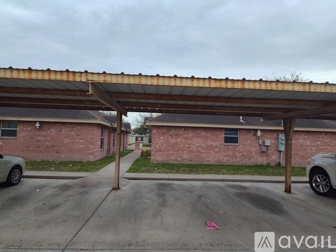 A carport with a rusted metal roof is in front of a brick house.