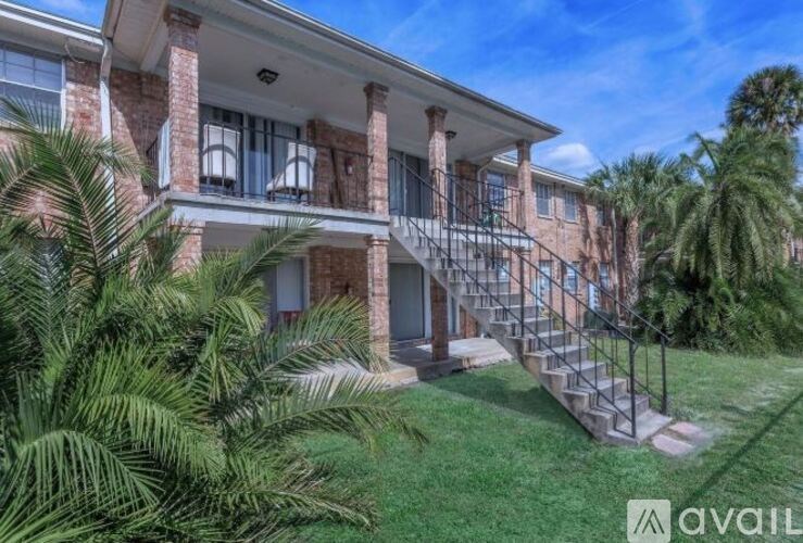 A building with a staircase leading to the entrance is surrounded by greenery.