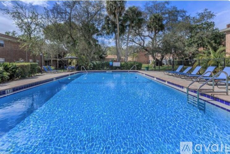 A large blue swimming pool surrounded by trees and lounge chairs.