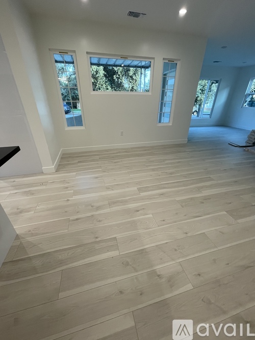 A spacious room with wooden flooring and windows.