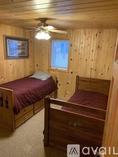 A bedroom with wooden walls and a bed with a burgundy cover.