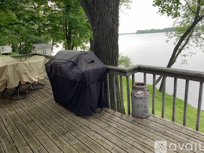 A patio with a table covered in a black umbrella and a white umbrella, a tree and a lake in the background.