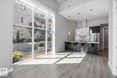 A modern kitchen with a dining table and chairs is visible through a glass wall.