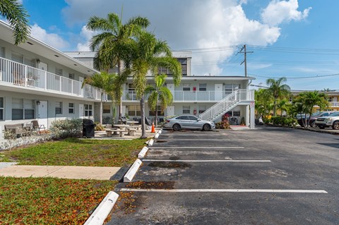 A parking lot in front of a white building with a silver car parked in the lot.